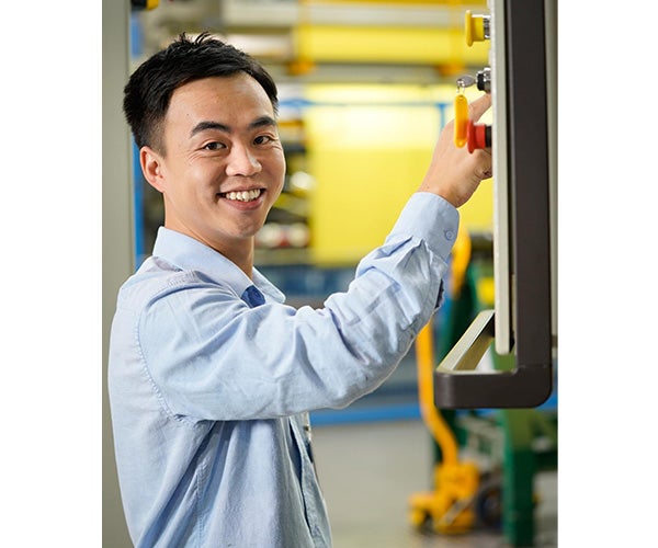 Ein Mitarbeiter steht lächelnd an einer Maschine.